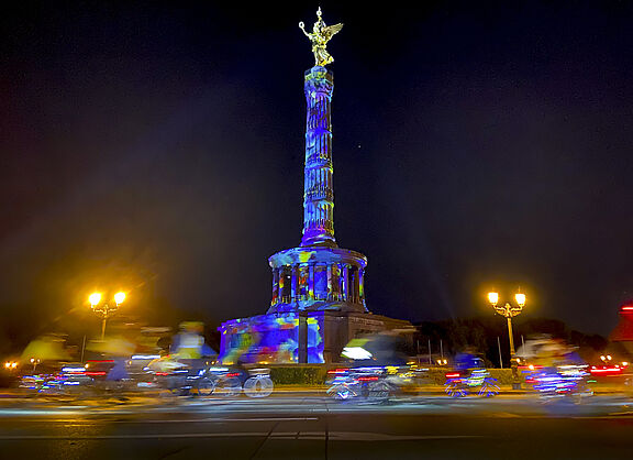 Lichterfahrt 2024 Menschen auf Fahrrädern fahren im Dunklen um die bunt angestrahlte Siegessäule